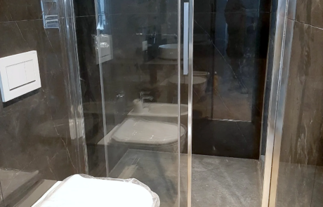 Bagno ristrutturato con box doccia in cristallo, rivestimento effetto pietra scura e sanitari sospesi