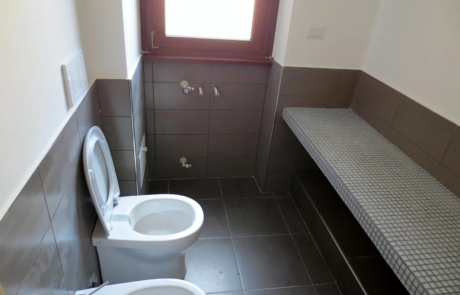 Bagno ristrutturato con sanitari, panca in muratura rivestita a mosaico e pavimento in gres scuro