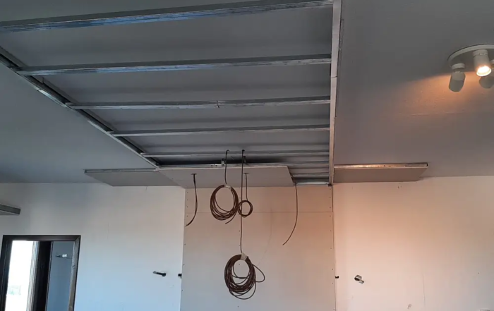 Cantiere di ristrutturazione in corso: struttura metallica del controsoffitto in cartongesso, parete in lastre con cavi elettrici in attesa di collegamento e scale da cantiere