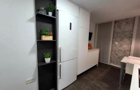 Cucina bianca con colonna frigo, mensole scure e parete effetto mattone