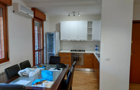 Cucina ristrutturata con zona pranzo, pensili bianchi e pavimento in legno