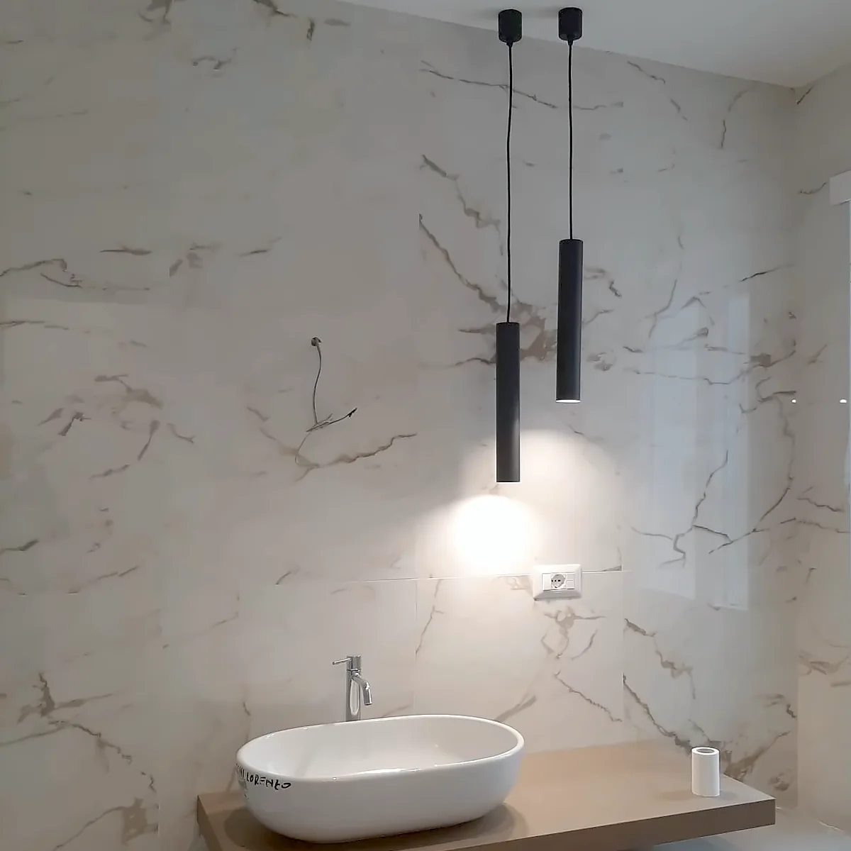 Ristrutturazione bagno Roma – bagno effetto marmo con lavabo d’appoggio Ristrutturazione bagno Roma di Edil Dima: rivestimento effetto marmo, lavabo d'appoggio su mensola in legno e lampade a sospensione nere